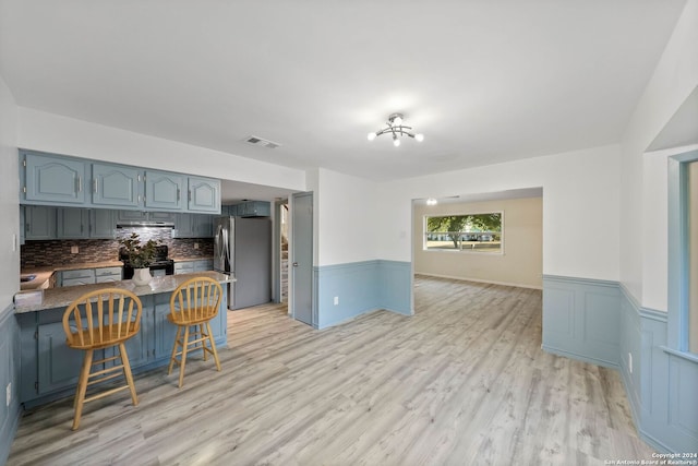 kitchen featuring stainless steel fridge, light hardwood / wood-style flooring, a kitchen breakfast bar, decorative backsplash, and kitchen peninsula