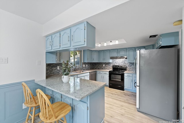 kitchen with light wood-type flooring, sink, kitchen peninsula, appliances with stainless steel finishes, and a kitchen breakfast bar