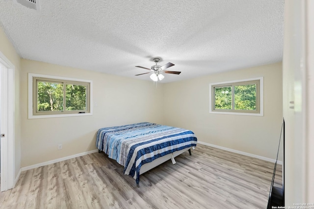 bedroom with a textured ceiling, multiple windows, ceiling fan, and light hardwood / wood-style flooring