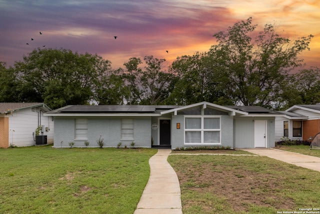 single story home featuring cooling unit, solar panels, and a lawn