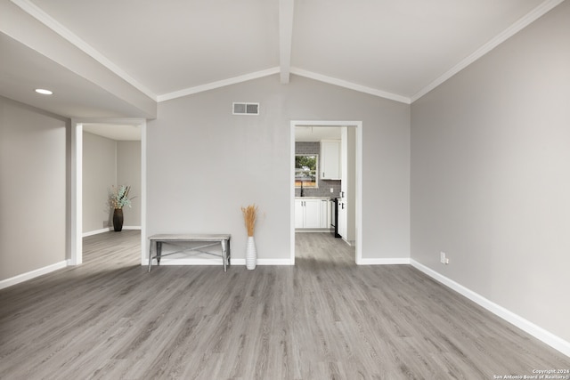 unfurnished living room with lofted ceiling with beams, ornamental molding, and light wood-type flooring