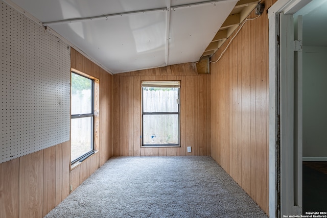 spare room with vaulted ceiling, plenty of natural light, carpet flooring, and wood walls