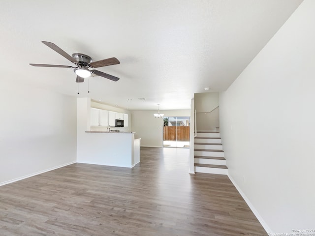 unfurnished living room featuring ceiling fan with notable chandelier, a textured ceiling, and dark hardwood / wood-style flooring