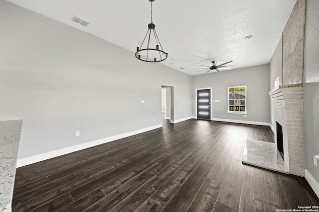 unfurnished living room with dark wood-type flooring, a brick fireplace, ceiling fan with notable chandelier, and a textured ceiling