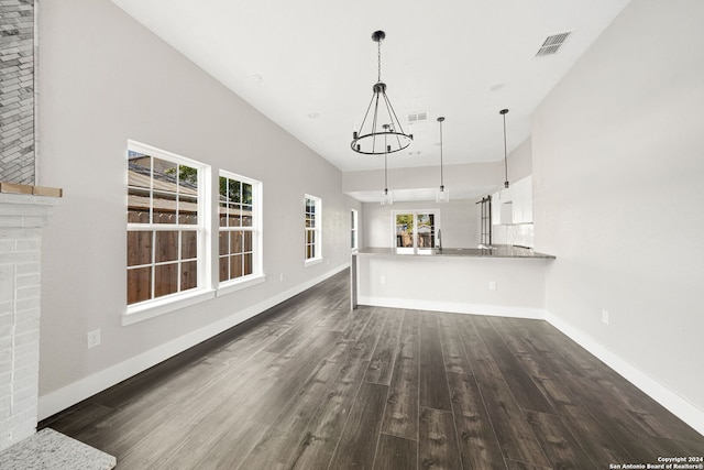 unfurnished living room with an inviting chandelier, a fireplace, plenty of natural light, and dark hardwood / wood-style flooring