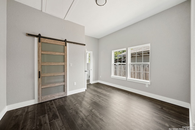 unfurnished bedroom with a barn door and dark hardwood / wood-style flooring