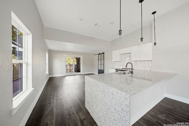 kitchen with a barn door, decorative light fixtures, sink, kitchen peninsula, and white cabinets