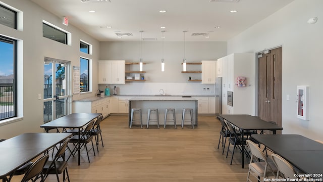 kitchen featuring light wood-type flooring, a center island, white cabinets, a breakfast bar, and hanging light fixtures