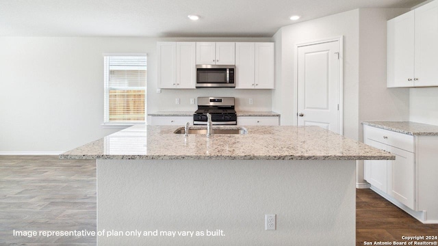 kitchen with wood-type flooring, an island with sink, appliances with stainless steel finishes, and white cabinetry