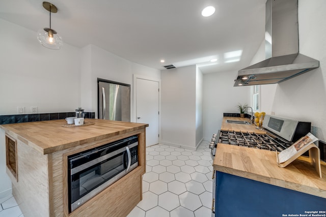 kitchen with blue cabinets, sink, wall chimney range hood, appliances with stainless steel finishes, and wood counters