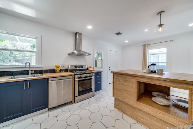 kitchen featuring blue cabinets, sink, decorative light fixtures, wall chimney range hood, and appliances with stainless steel finishes