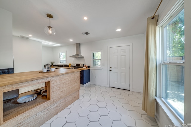 kitchen featuring stainless steel stove, sink, pendant lighting, wall chimney range hood, and wood counters