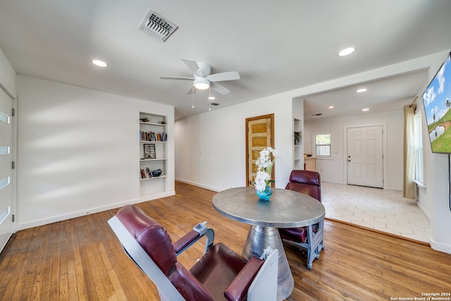 living room featuring built in features, hardwood / wood-style floors, and ceiling fan