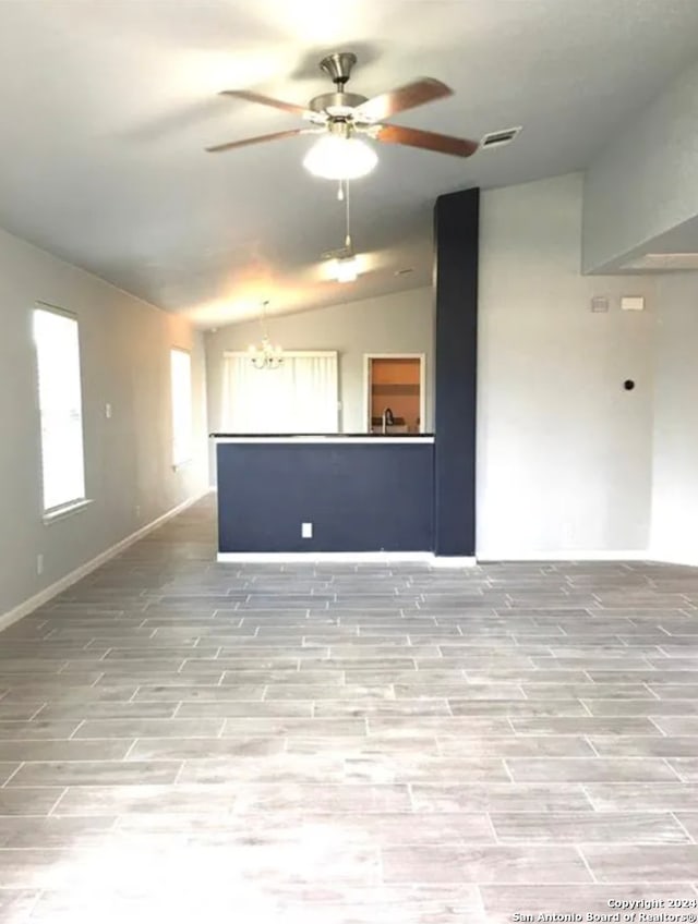 unfurnished room with ceiling fan with notable chandelier, vaulted ceiling, and light wood-type flooring