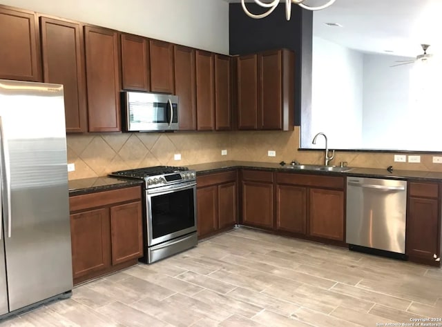 kitchen with ceiling fan, stainless steel appliances, sink, light hardwood / wood-style floors, and dark stone counters