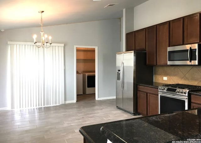 kitchen with lofted ceiling, hanging light fixtures, washing machine and clothes dryer, stainless steel appliances, and light hardwood / wood-style floors