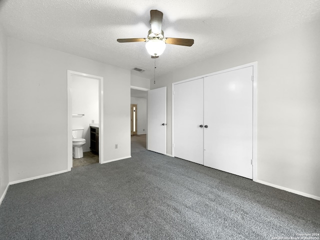 unfurnished bedroom featuring ceiling fan, a closet, dark carpet, ensuite bath, and a textured ceiling