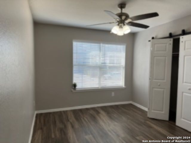 interior space with ceiling fan, dark wood-type flooring, and a barn door