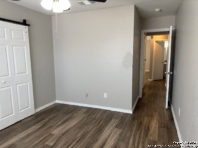 unfurnished bedroom with a barn door and dark hardwood / wood-style flooring