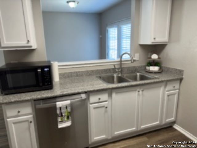 kitchen featuring dark wood-type flooring, sink, light stone counters, dishwasher, and white cabinets