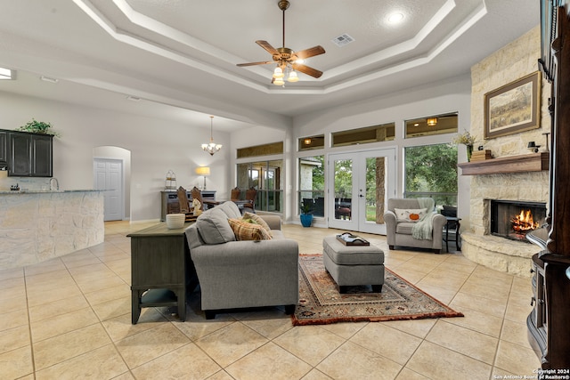 tiled living room featuring french doors, a raised ceiling, sink, ceiling fan with notable chandelier, and a fireplace