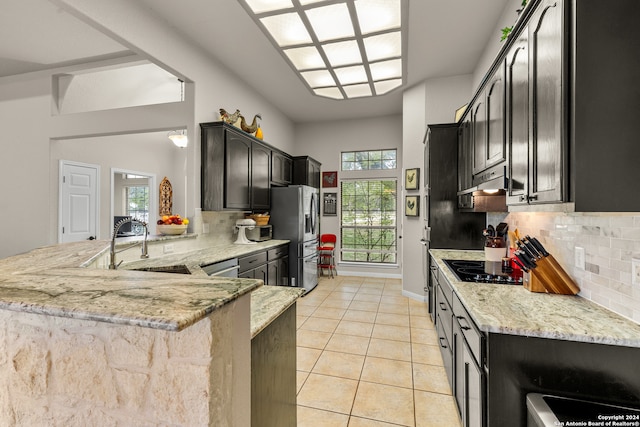 kitchen with tasteful backsplash, light stone countertops, sink, kitchen peninsula, and stainless steel refrigerator with ice dispenser