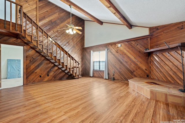 unfurnished living room with ceiling fan, wood walls, a textured ceiling, light hardwood / wood-style flooring, and high vaulted ceiling