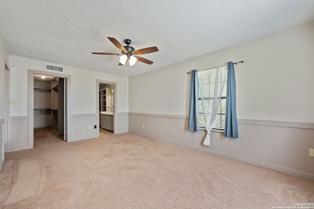 unfurnished bedroom featuring a wainscoted wall, a textured ceiling, visible vents, light colored carpet, and a walk in closet
