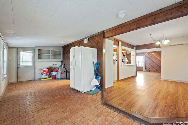 interior space featuring wood-type flooring, an inviting chandelier, wooden walls, and white refrigerator with ice dispenser