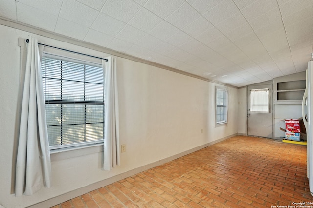 unfurnished room featuring ornamental molding and brick floor