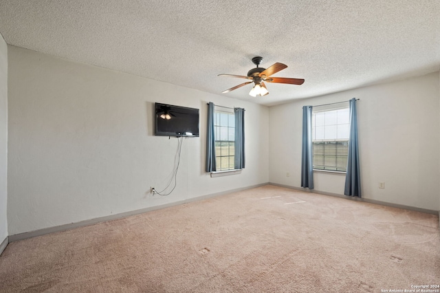 carpeted spare room featuring baseboards, a textured ceiling, ceiling fan, and a healthy amount of sunlight