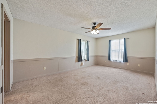 spare room featuring ceiling fan, light colored carpet, and a textured ceiling