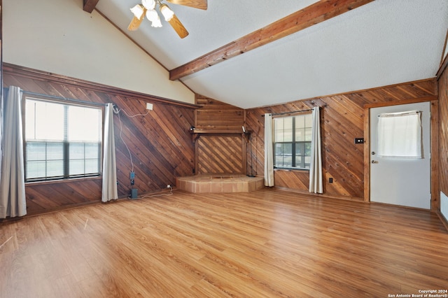 unfurnished living room featuring ceiling fan, wooden walls, vaulted ceiling with beams, and light hardwood / wood-style floors