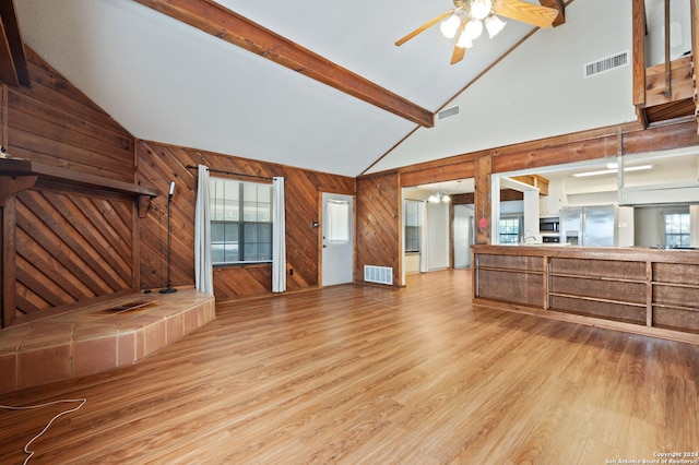 unfurnished living room with ceiling fan, beam ceiling, wooden walls, light hardwood / wood-style flooring, and high vaulted ceiling