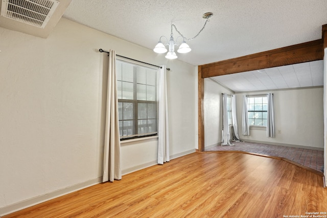 unfurnished room featuring vaulted ceiling with beams, a notable chandelier, light wood-type flooring, and a textured ceiling