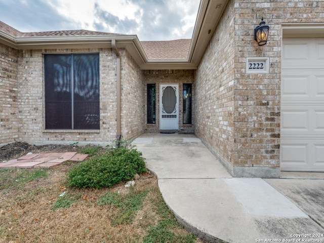 property entrance with brick siding, roof with shingles, and a garage