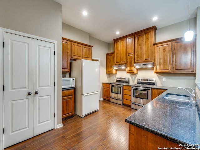 kitchen with under cabinet range hood, white appliances, a sink, and brown cabinets