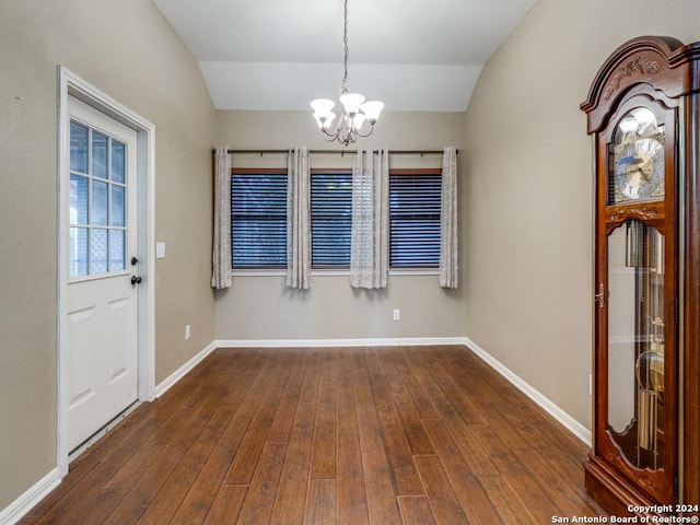 unfurnished dining area with dark wood-style flooring, a notable chandelier, vaulted ceiling, and baseboards