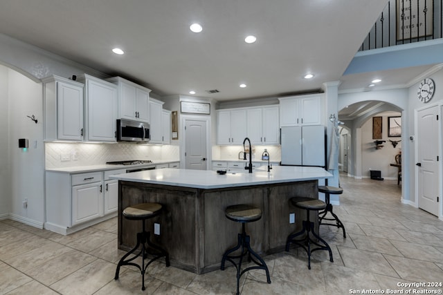 kitchen with white cabinets, an island with sink, appliances with stainless steel finishes, a kitchen breakfast bar, and crown molding