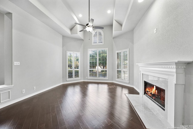 unfurnished living room featuring a high end fireplace, ceiling fan, a towering ceiling, and dark hardwood / wood-style floors