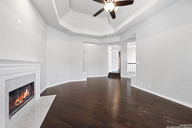 unfurnished living room featuring ceiling fan, a fireplace, a raised ceiling, and hardwood / wood-style floors