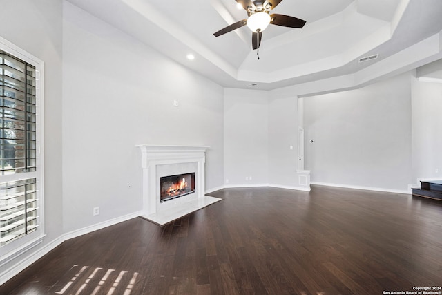 unfurnished living room featuring dark wood-type flooring, a tray ceiling, a fireplace, and ceiling fan