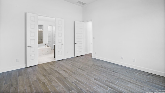 unfurnished bedroom featuring hardwood / wood-style floors, a high ceiling, and ensuite bath