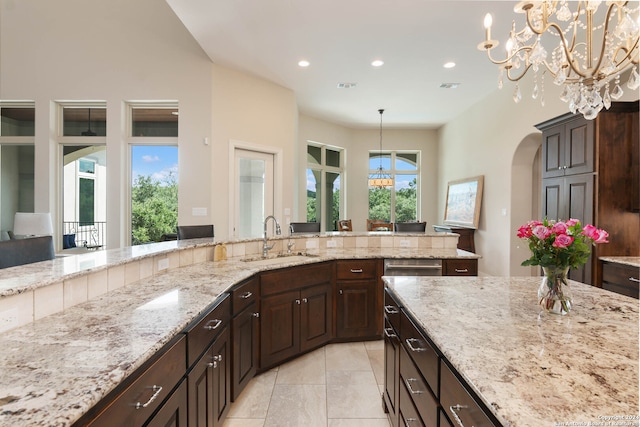 kitchen featuring light stone counters, pendant lighting, a chandelier, and sink