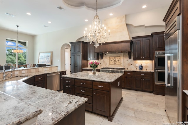 kitchen with light stone counters, hanging light fixtures, sink, a kitchen island, and stainless steel appliances