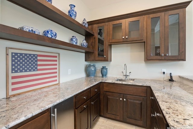 kitchen with light stone counters, light tile patterned floors, dark brown cabinetry, and sink