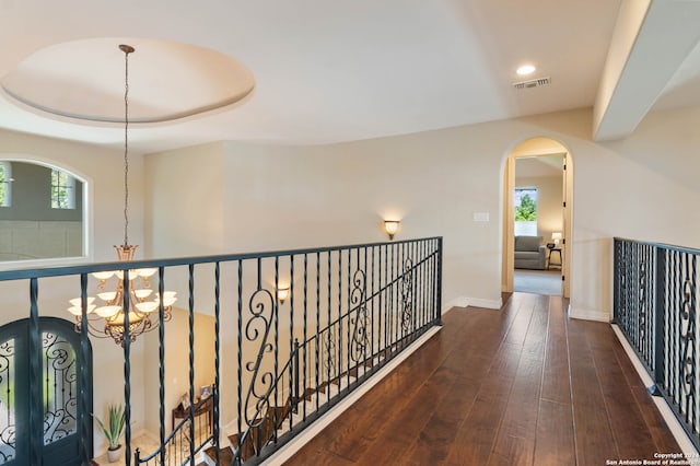 corridor with a notable chandelier, a raised ceiling, and dark wood-type flooring