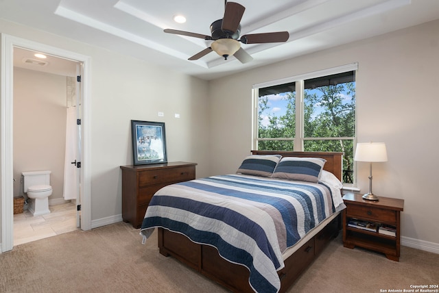 bedroom featuring ceiling fan, light colored carpet, a tray ceiling, and ensuite bath