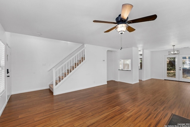 unfurnished living room featuring french doors, ceiling fan with notable chandelier, and dark hardwood / wood-style floors