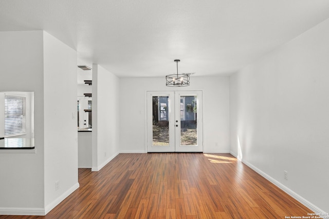 empty room featuring an inviting chandelier, dark hardwood / wood-style flooring, and french doors